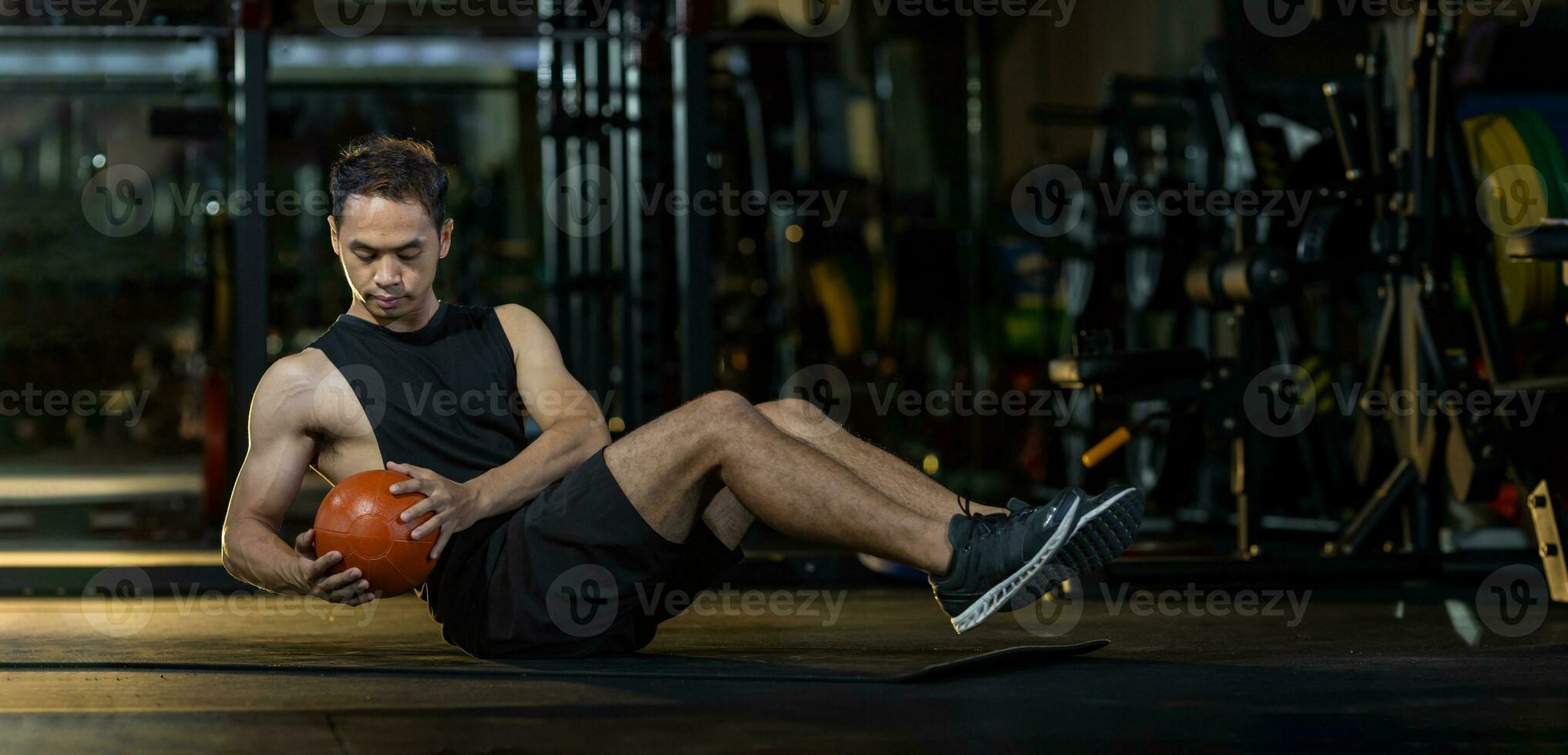 Asian man workout in gym doing seated oblique twist exercise with weight medicine ball on floor which strengthen the abs abdominal and the core body muscle photo