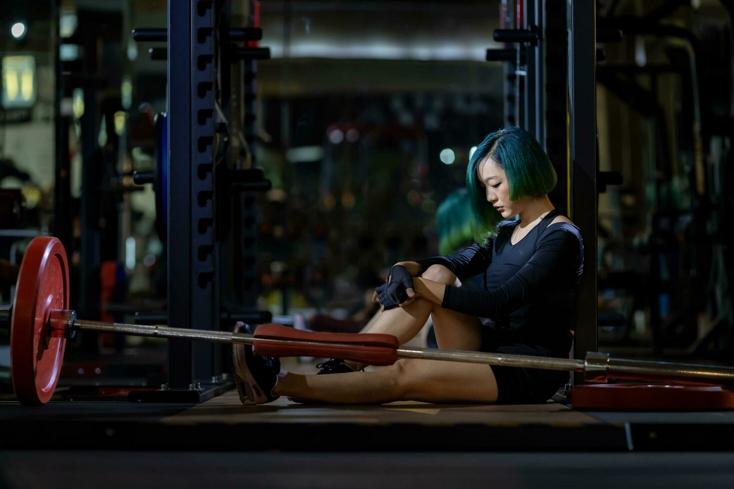 Asian woman is facing overtraining syndrome after weight training workout inside gym with dark background for exercising and fitness concept photo