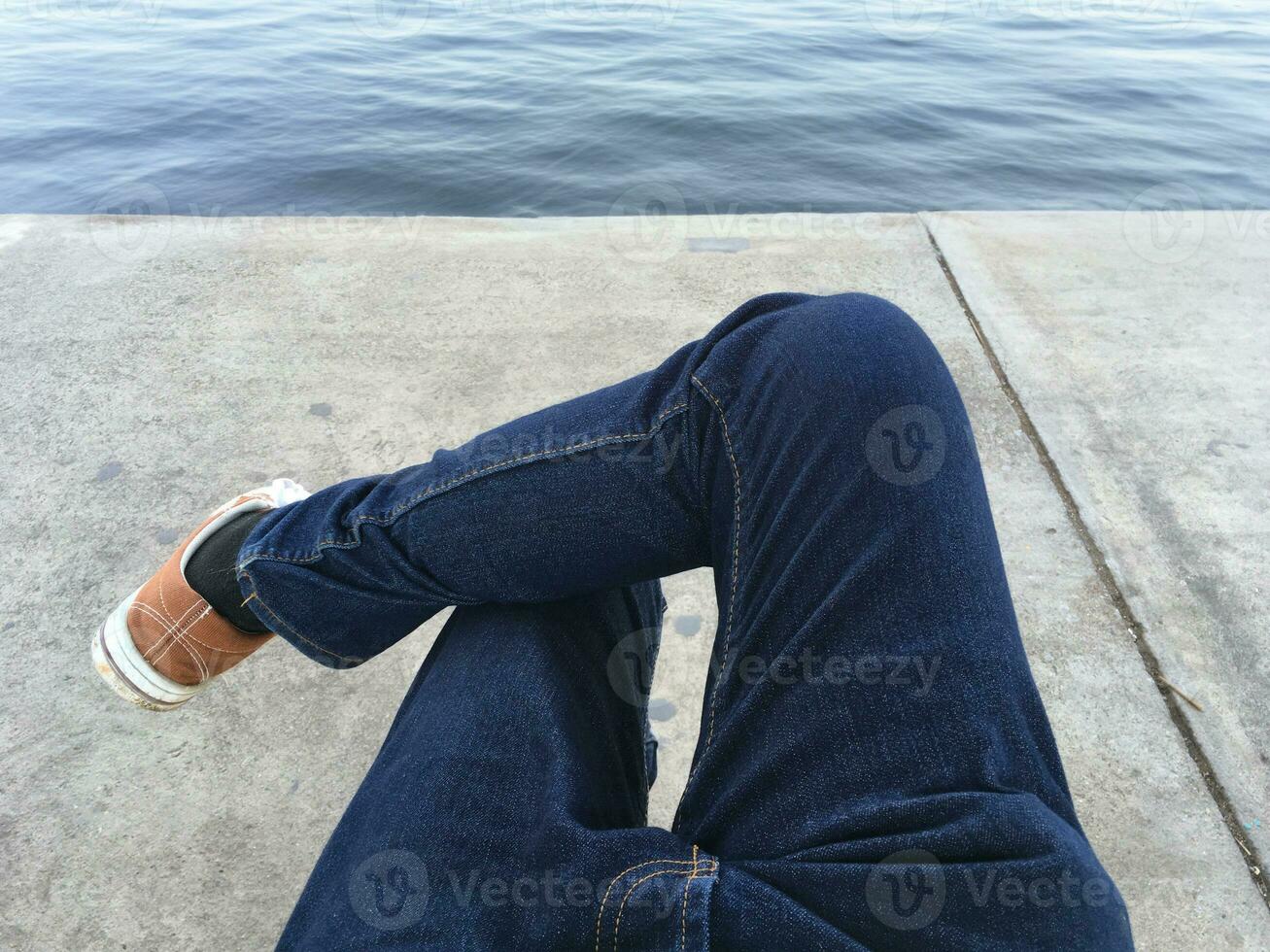 young man legs in jeans sitting near the river photo