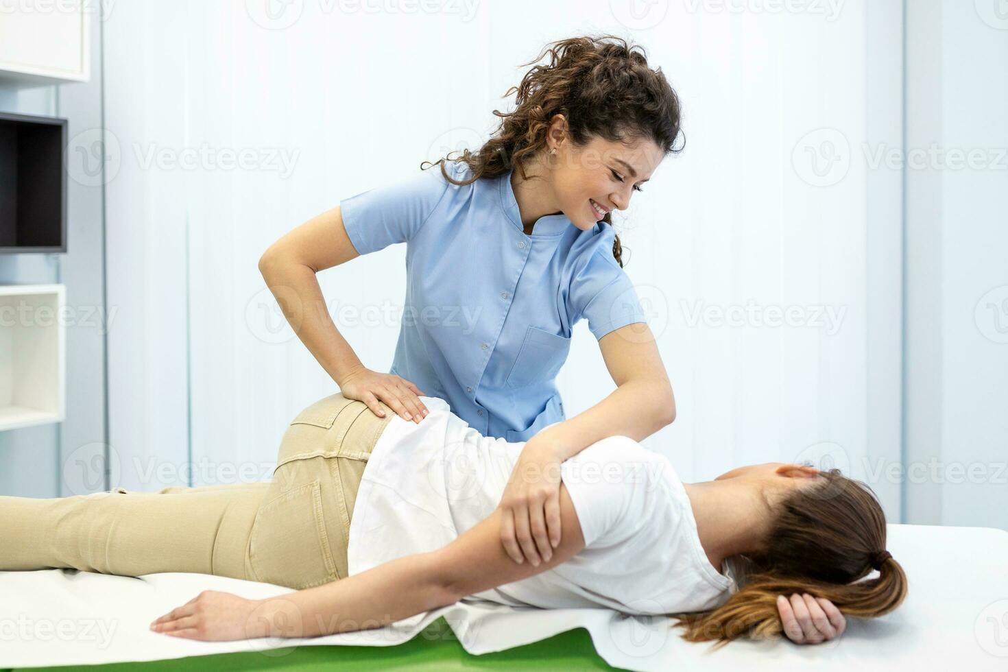 Young woman doctor chiropractor or osteopath fixing lying womans back with hands movements during visit in manual therapy clinic. Professional chiropractor during work photo