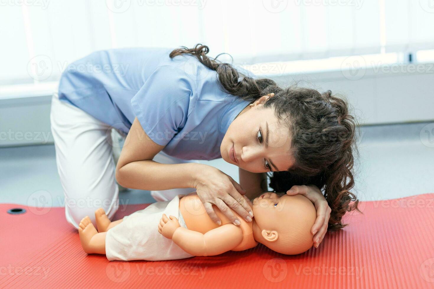 CPR practitioner examining airway passages on infant dummy. Model dummy lays on table and two doctors practice first aid. photo