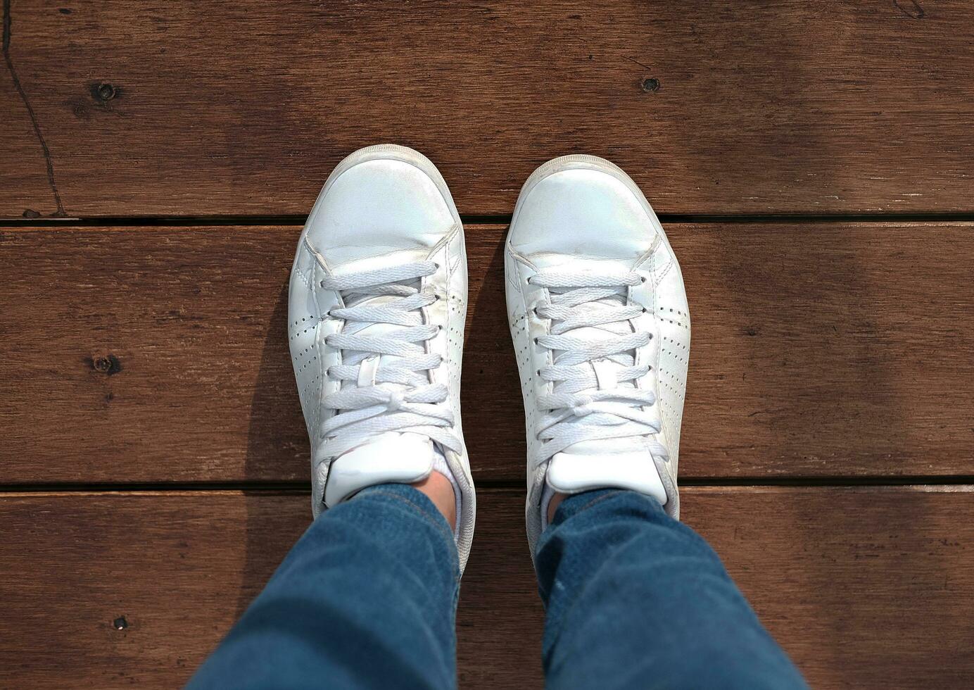 Top view of white sneakers and Blue jeans on woman legs on wood floor background photo