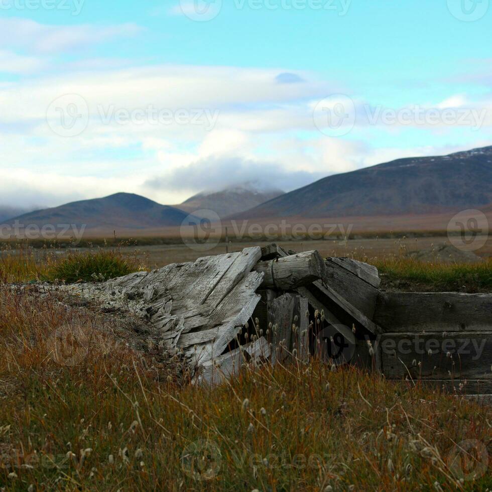 A wooden building destroyed over the years against a background of tundra and mountains with clouds photo