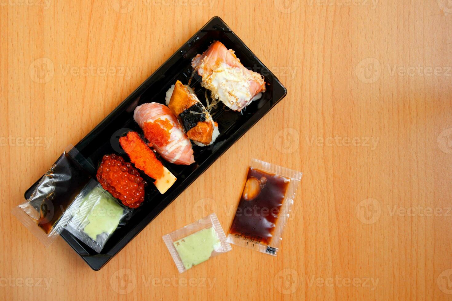 Sushi en rectángulo forma negro el plastico caja y wasabi, soja salsa en brillante marrón madera. foto