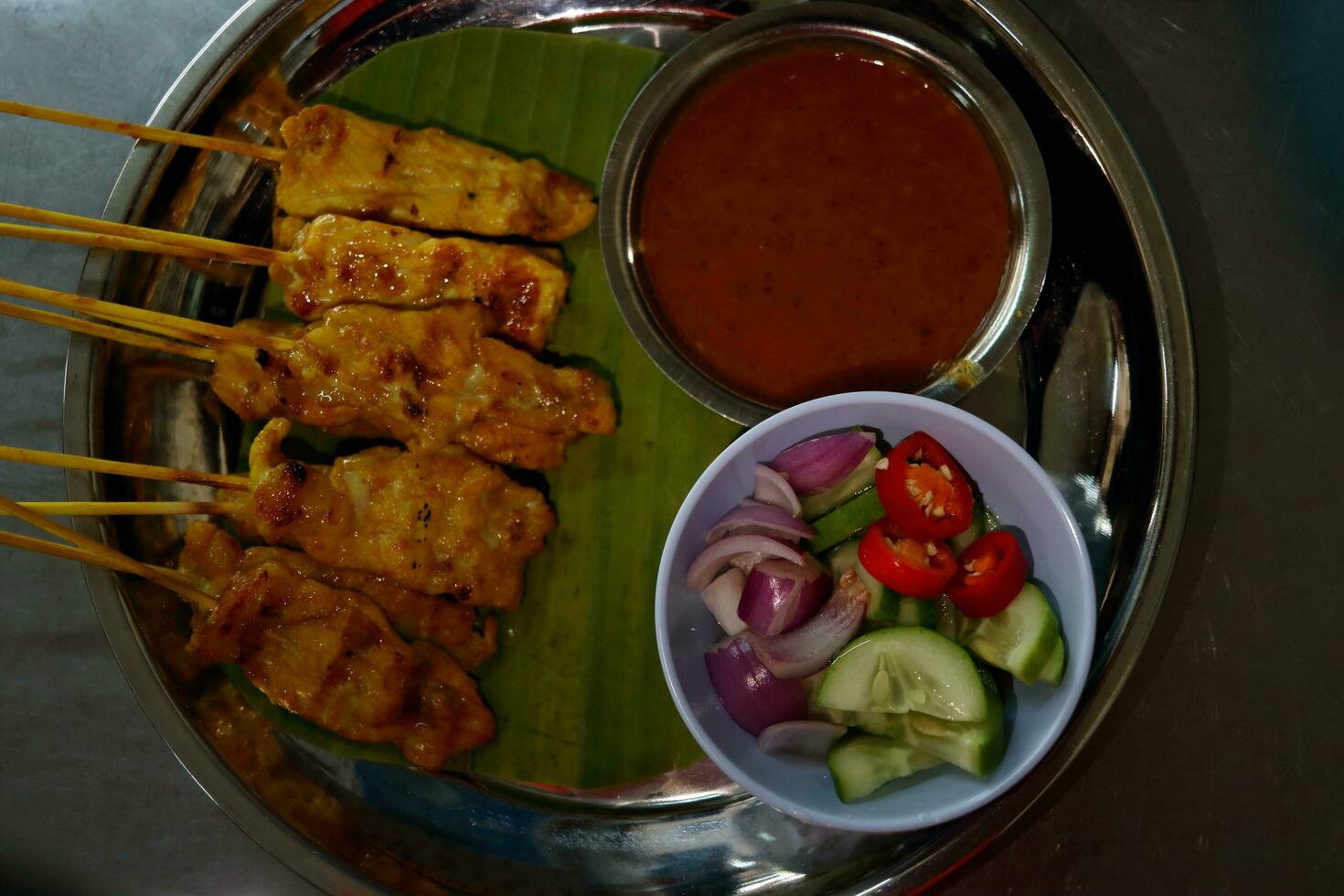 Pork satay stick and peanut sauce with vegetable marinated in vinegar on round metal plate, Thailand. photo