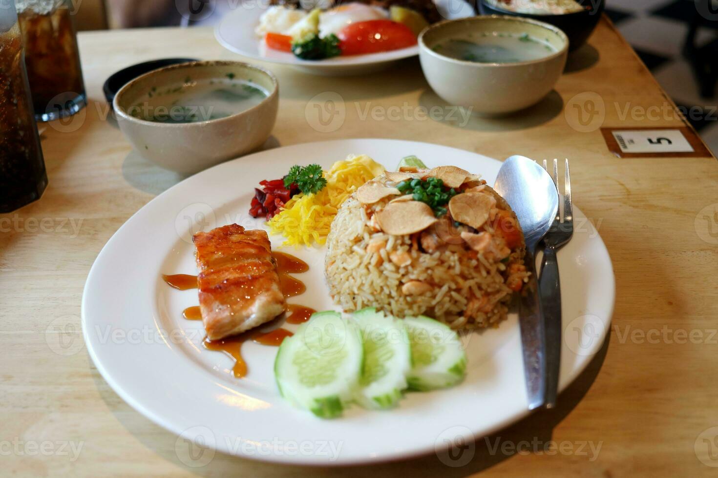 salmón frito arroz en blanco plato con salmón filete A la parrilla , Pepino rebanada, tortilla, chile y sopa en madera mesa, tailandia foto