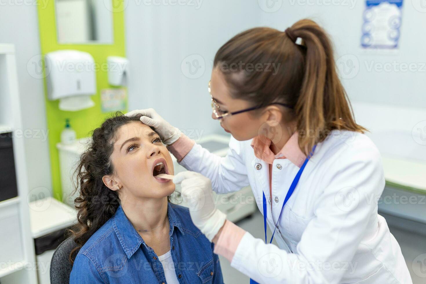 Otolaryngologist using inspection spatula to examines mature woman's throat. ENT doctor doing throat exam of a woman. patient opened her mouth to throat check-up photo