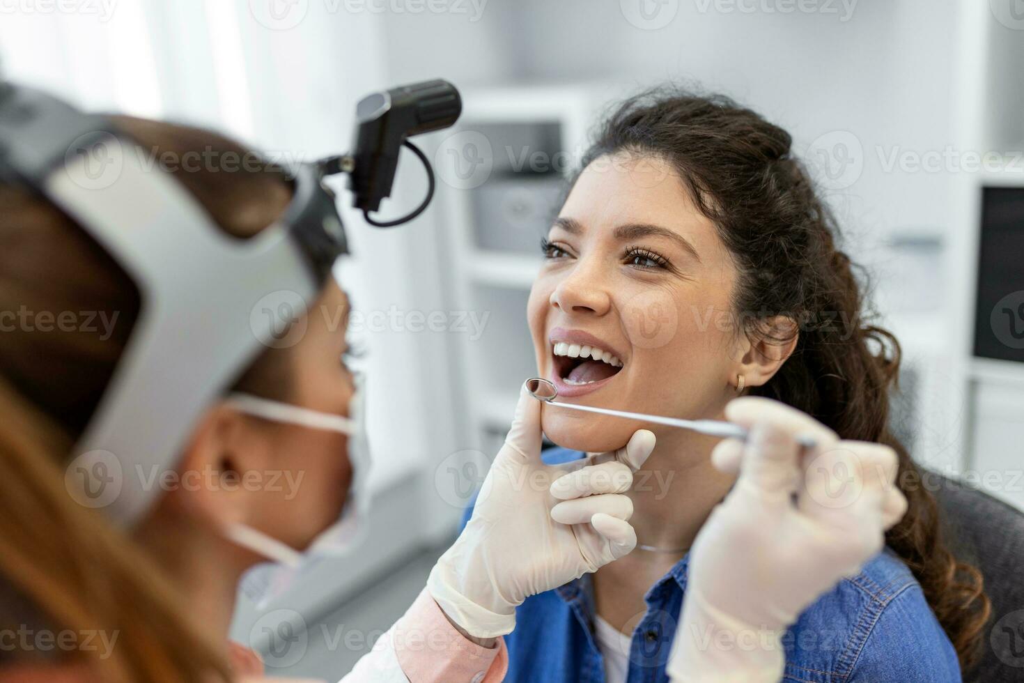 Female patient opening her mouth for the doctor to look in her throat. Female doctor examining sore throat of patient in clinic. Otolaryngologist examines sore throat of patient. photo