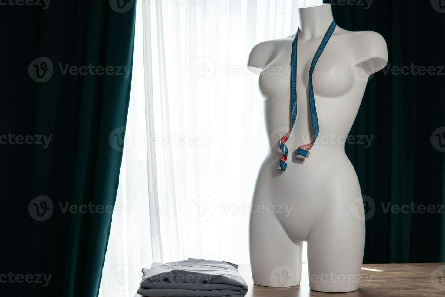 White modern mannequin or dressmakers dummy with gray fabric and hanging measuring tape photo