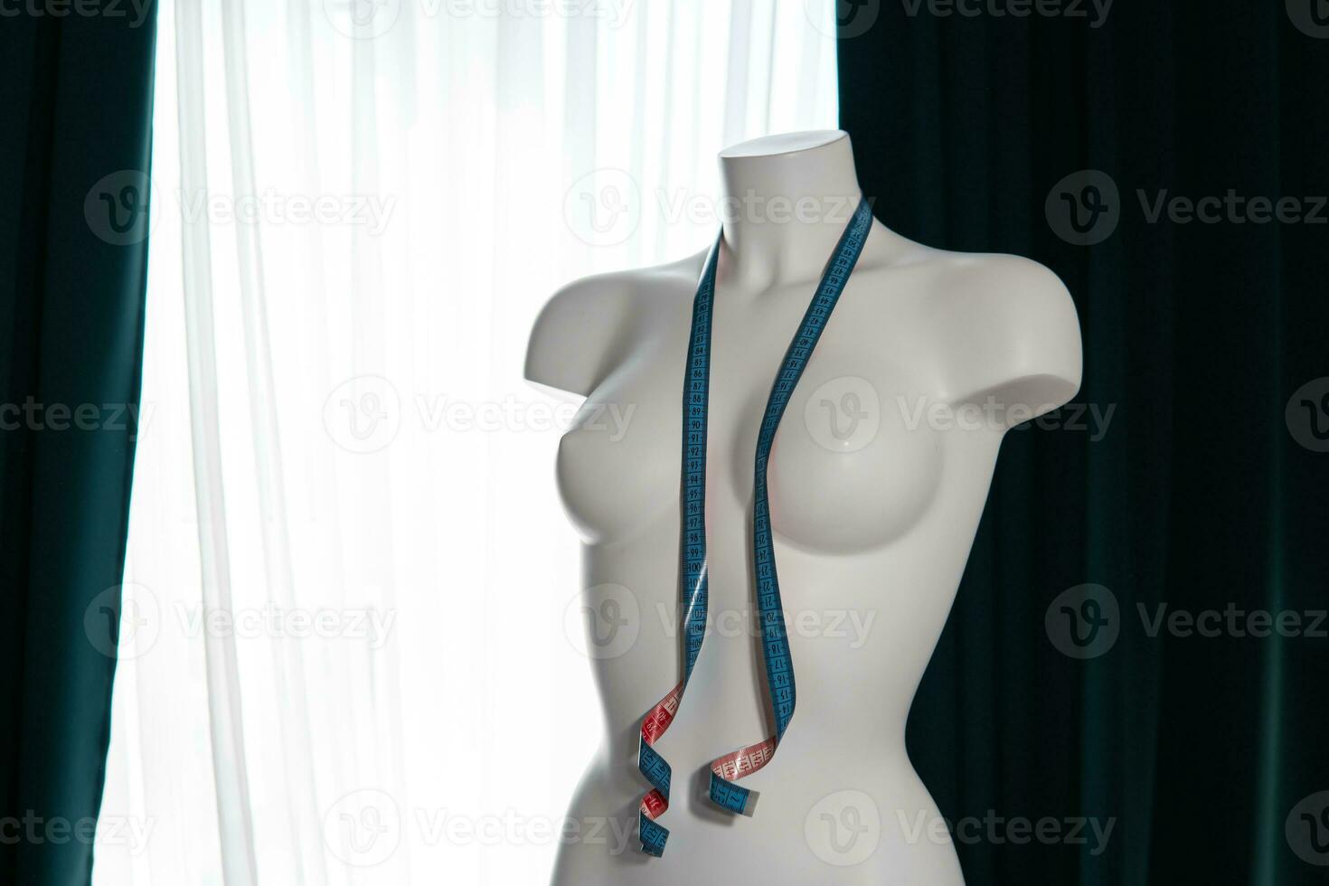 White modern mannequin or dressmakers dummy with gray fabric and hanging measuring tape photo