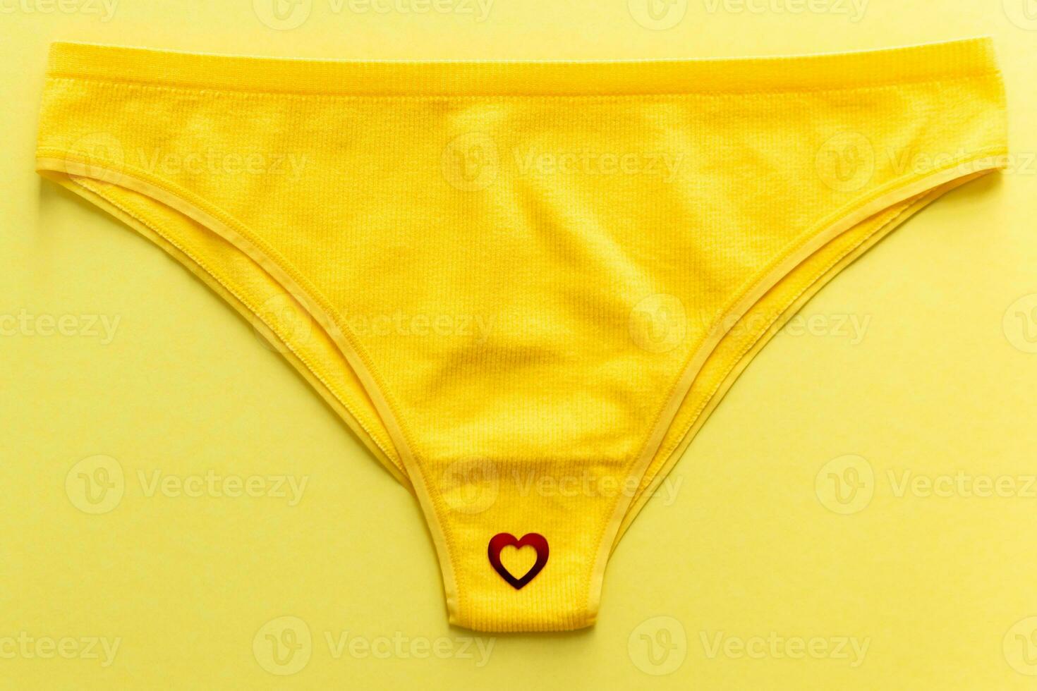 Top view of colorful females panties with red heart confetti on  yellow background photo