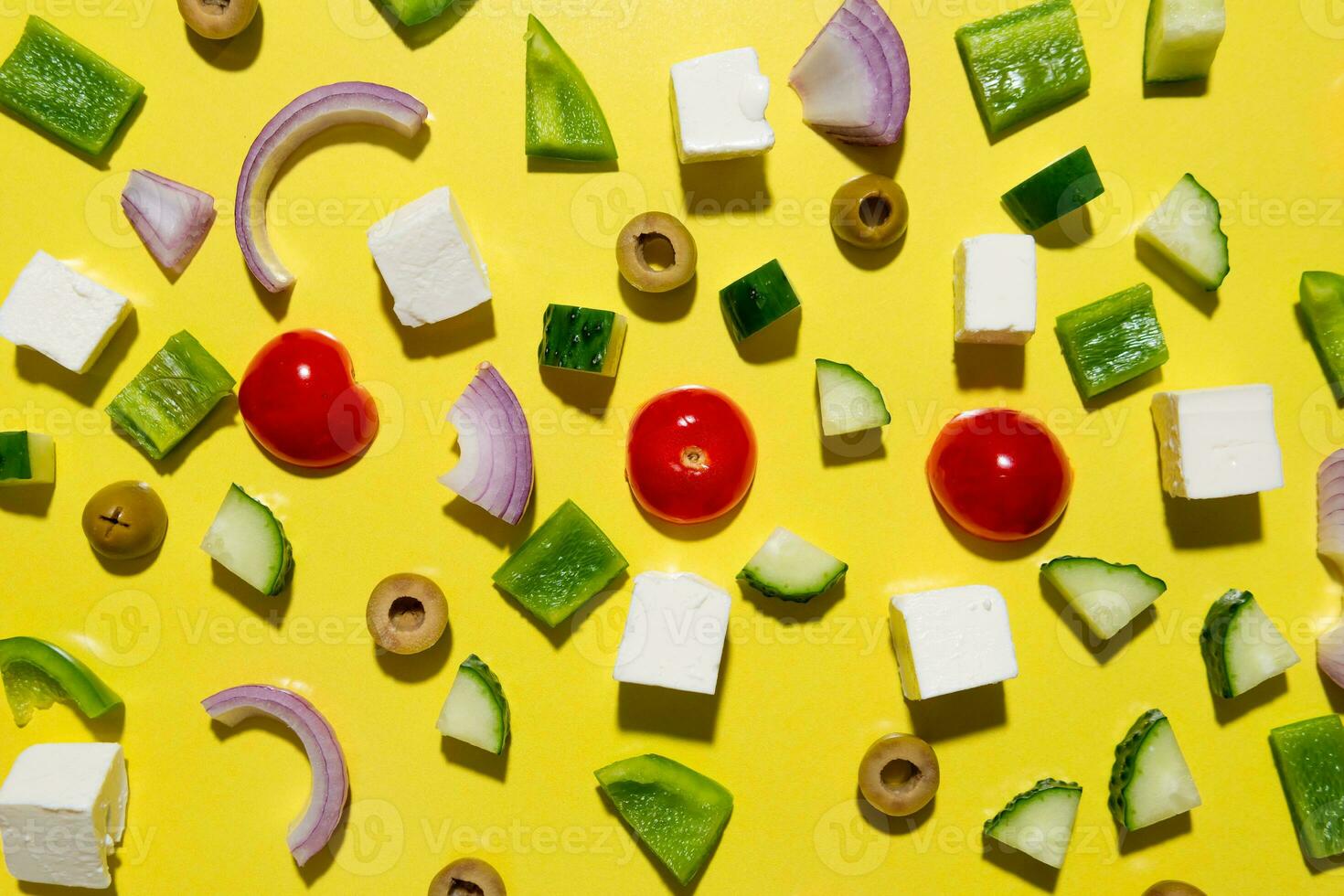 Ingredients for traditional greek salad with fresh vegetables, feta cheese and olives on yellow background photo