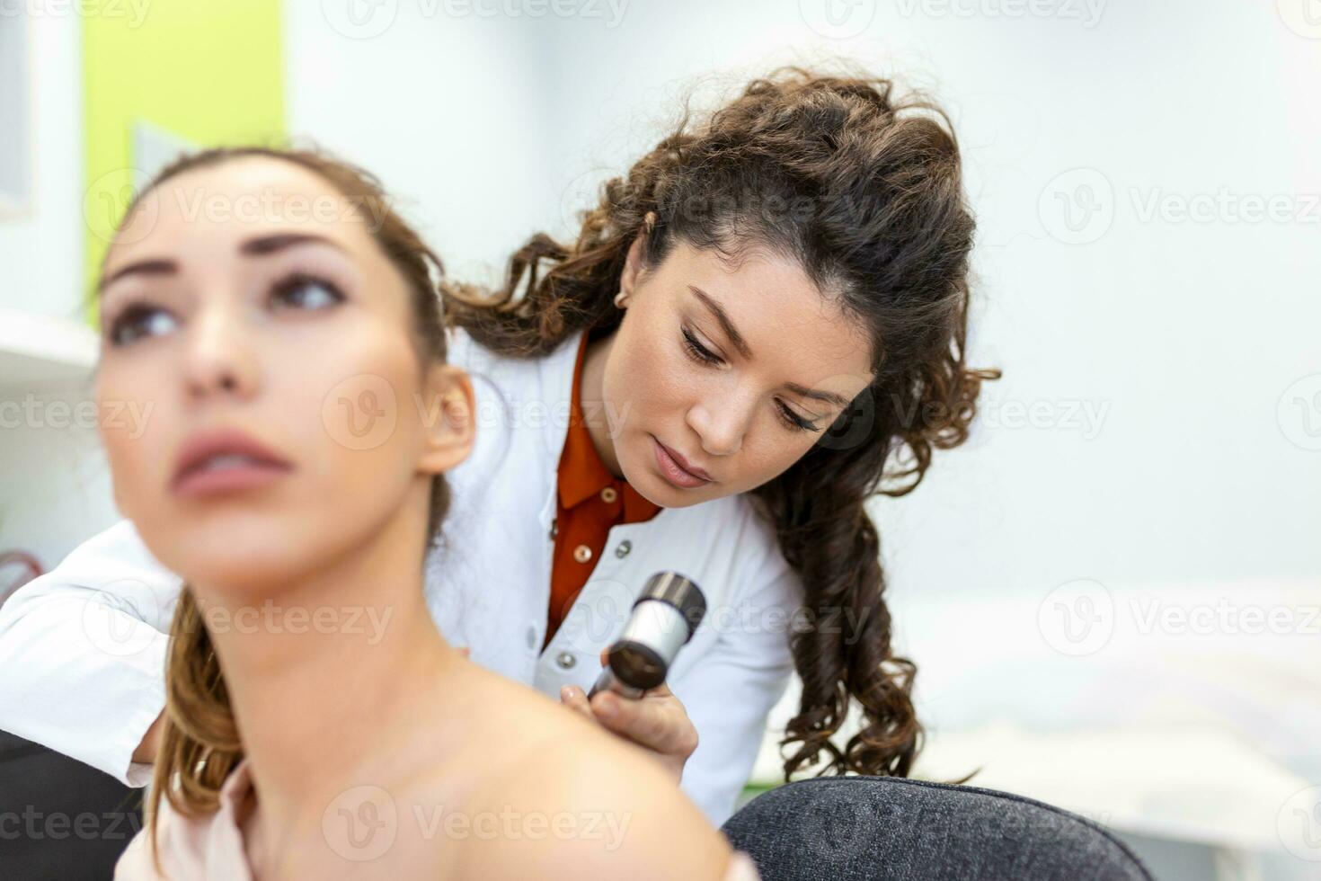 Dermatologist in latex gloves holding dermatoscope while examining attractive patient with skin disease. Female dermatologist examining patient with dermascope, looking for signs of skin cancer. photo