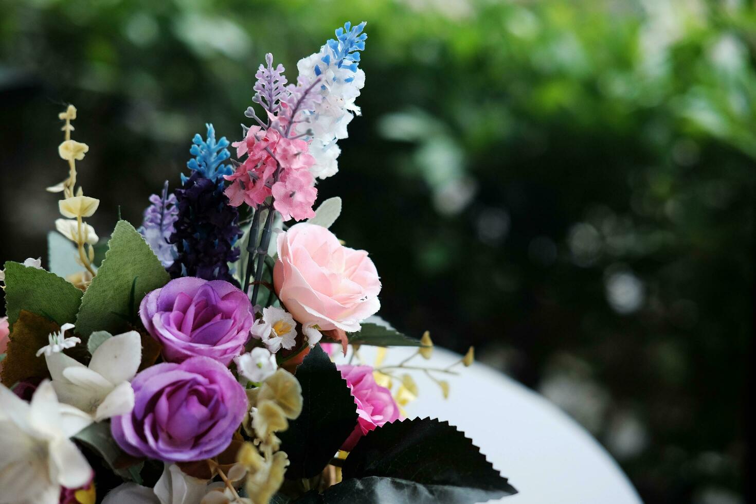 Beautiful plastic blooming rose flowers and flora bouquet on white table decorated in garden photo