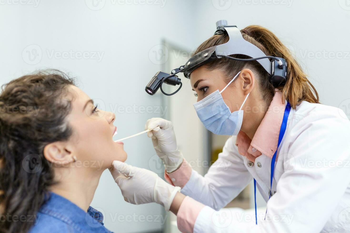 Doctor using inspection spatula to examine patient throat. ENT doctor doing throat exam of a woman. patient opened her mouth to throat check-up photo