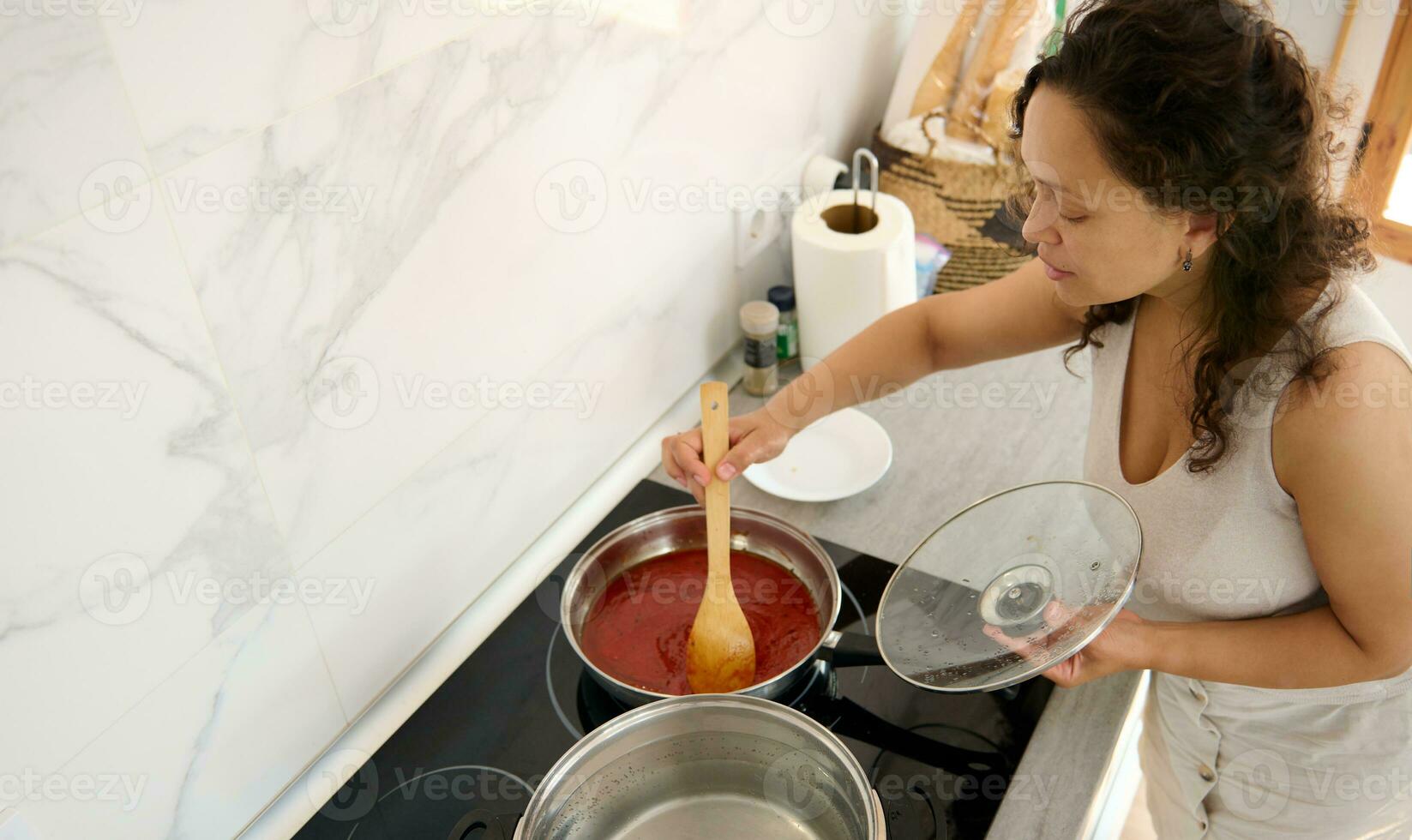 gastos generales ver encantador italiano mujer en pie por eléctrico cocina, mezcla ingredientes en un fritura pan mientras Cocinando cena foto