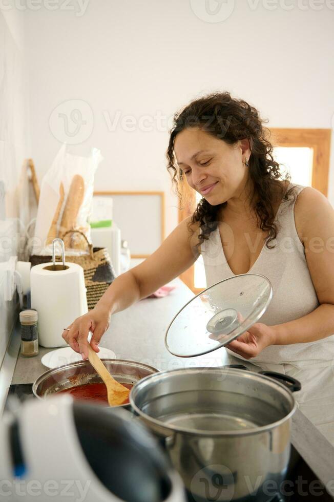 contento ama de casa Cocinando en el hogar cocina, mezcla Fresco ingredientes mientras preparando un tomate salsa foto