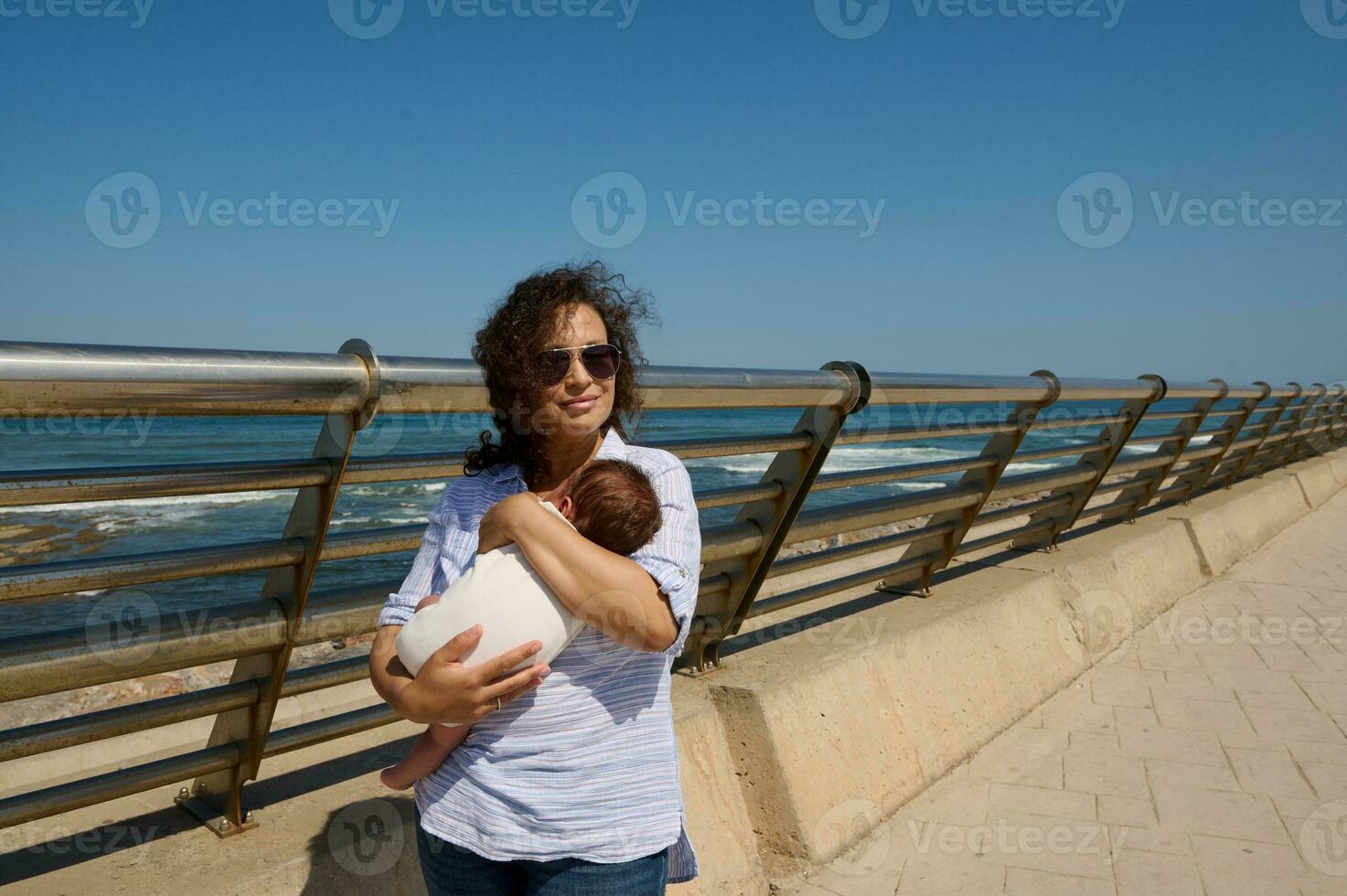 Beautiful woman in sunglasses, happy loving mom enjoying the stroll with her newborn baby on a beautiful sunny day photo