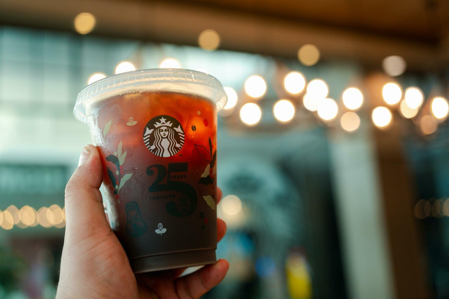 Bangkok, Thailand - October 16, 2023 Man holding a cup of  reusable cup cold  Americano 25th Anniversary, Starbucks Thailand. Limited-edition photo