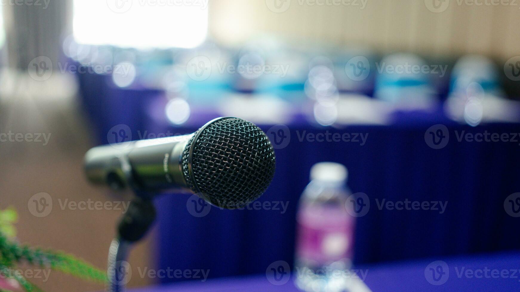 Microphone on the speaker table over the abstract blurred photo of the conference hall.