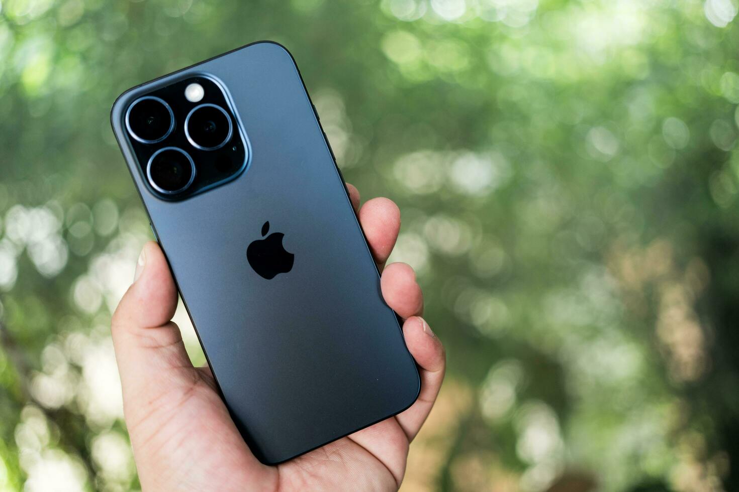 Bangkok, Thailand - October 15, 2023 New Apple iPhone 15 Pro blue titanium in male hand on a nature defocused blur background. photo