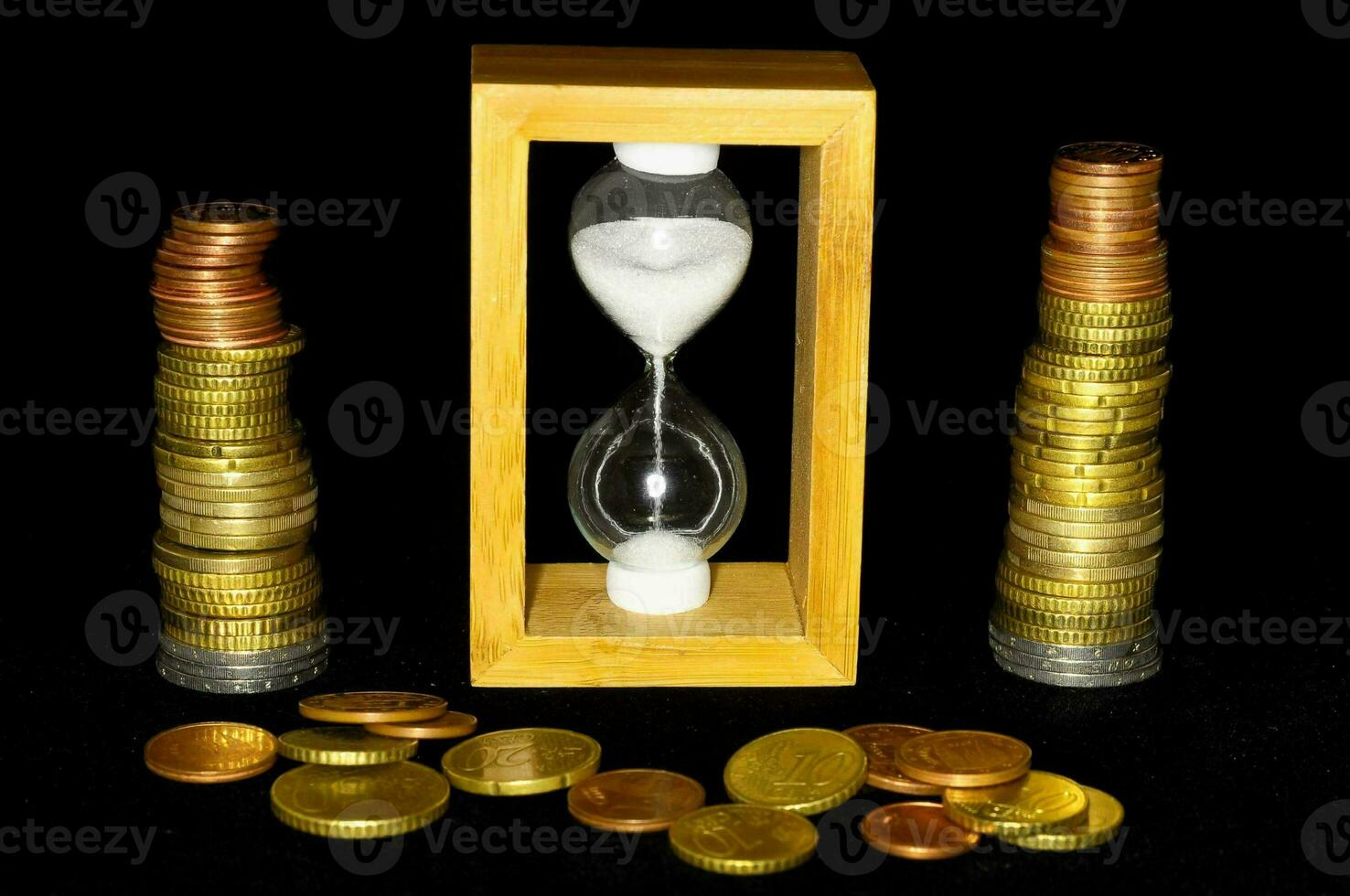 an hourglass and coins on a black background photo