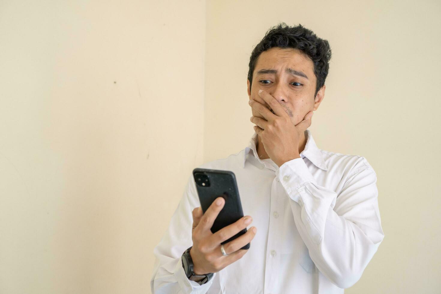 Indonesian man wear white clothes surprised when looking the smartphone. photo