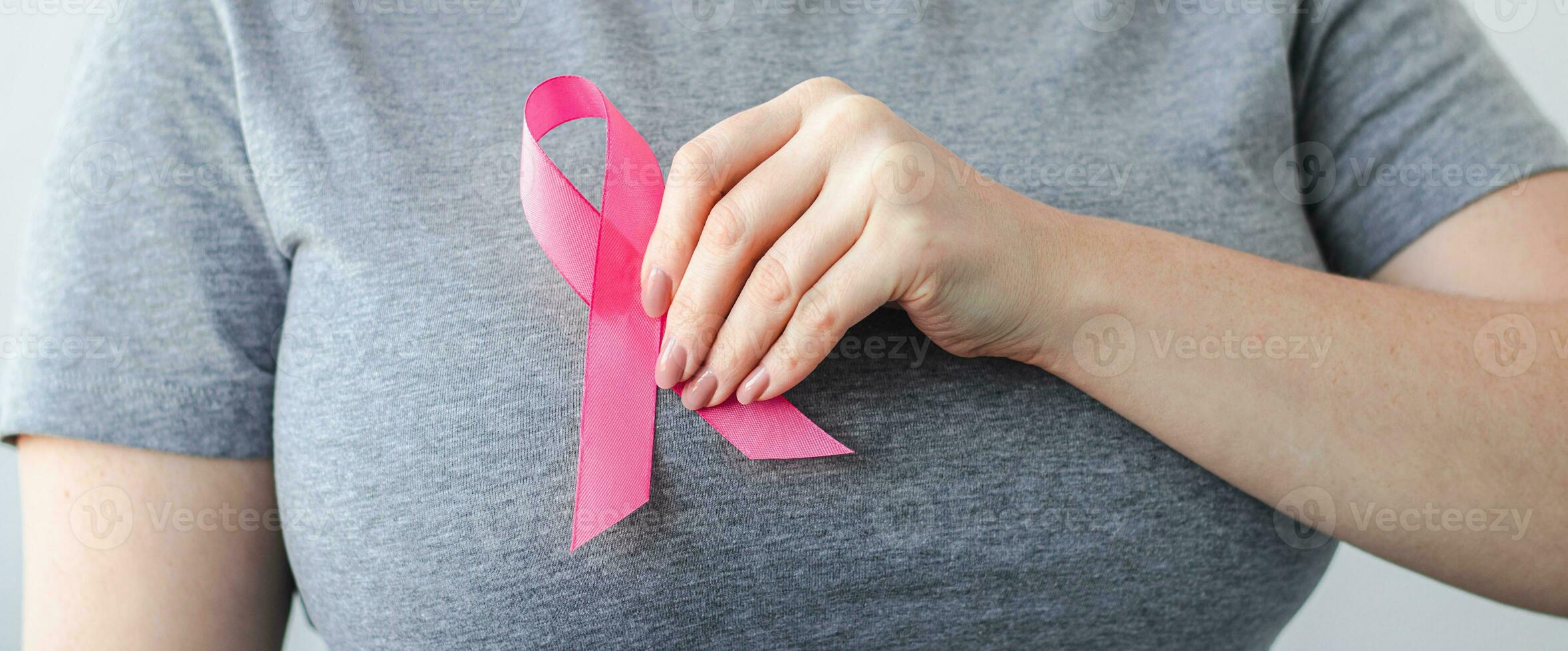 Woman in gray t-shirt attaches pink ribbon to her chest. Breast Cancer Awareness Month. Promoting campaign against cancer. photo