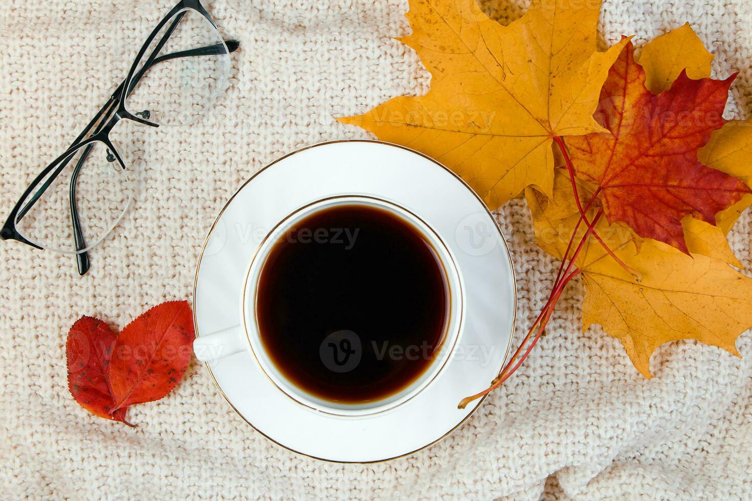 Cup of hot strong coffee and fallen leaf. Autumn morning concept. Warm beverage for cold weather and knitted sweater. photo