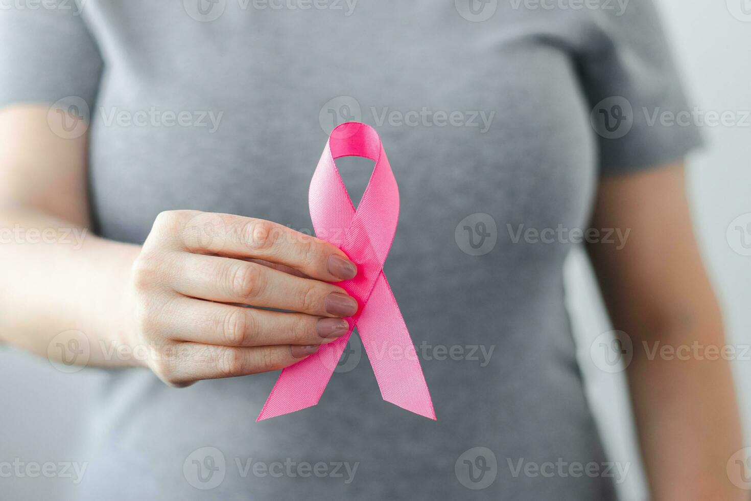 Woman in gray t-shirt holds pink ribbon in her hands. Breast Cancer Awareness Month. Supporting and promoting campaign against cancer. photo