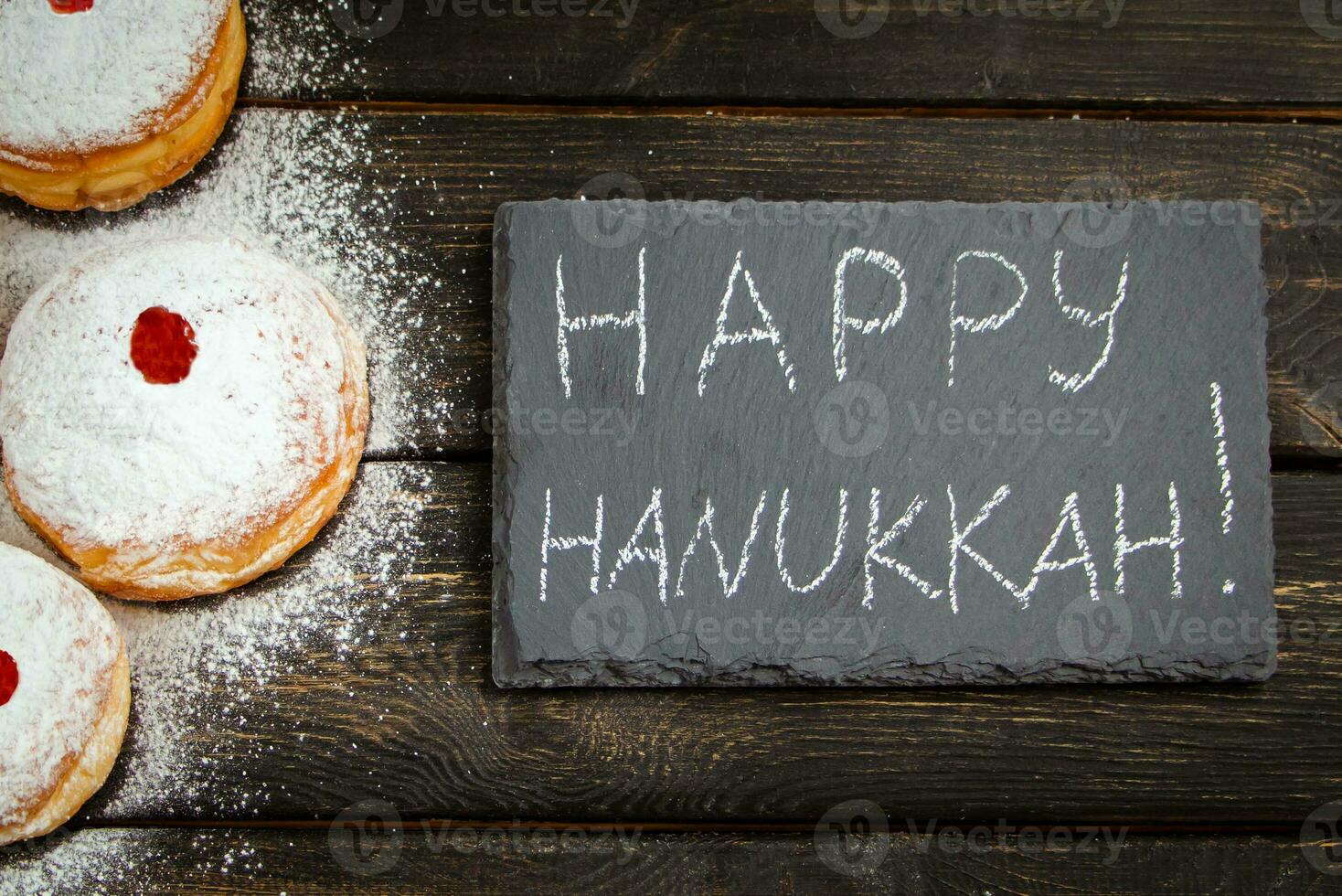 Happy Hanukkah. Traditional dessert Sufganiyot on dark wooden background. Donuts, candles and gifts. Celebrating Jewish holiday. photo