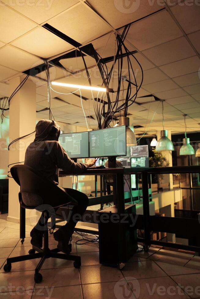 Cyberattack, hacker running malware code on computer, hacking database, stealing electronic information. Cyberterrorism, internet criminal in hoodie breaking into online server photo