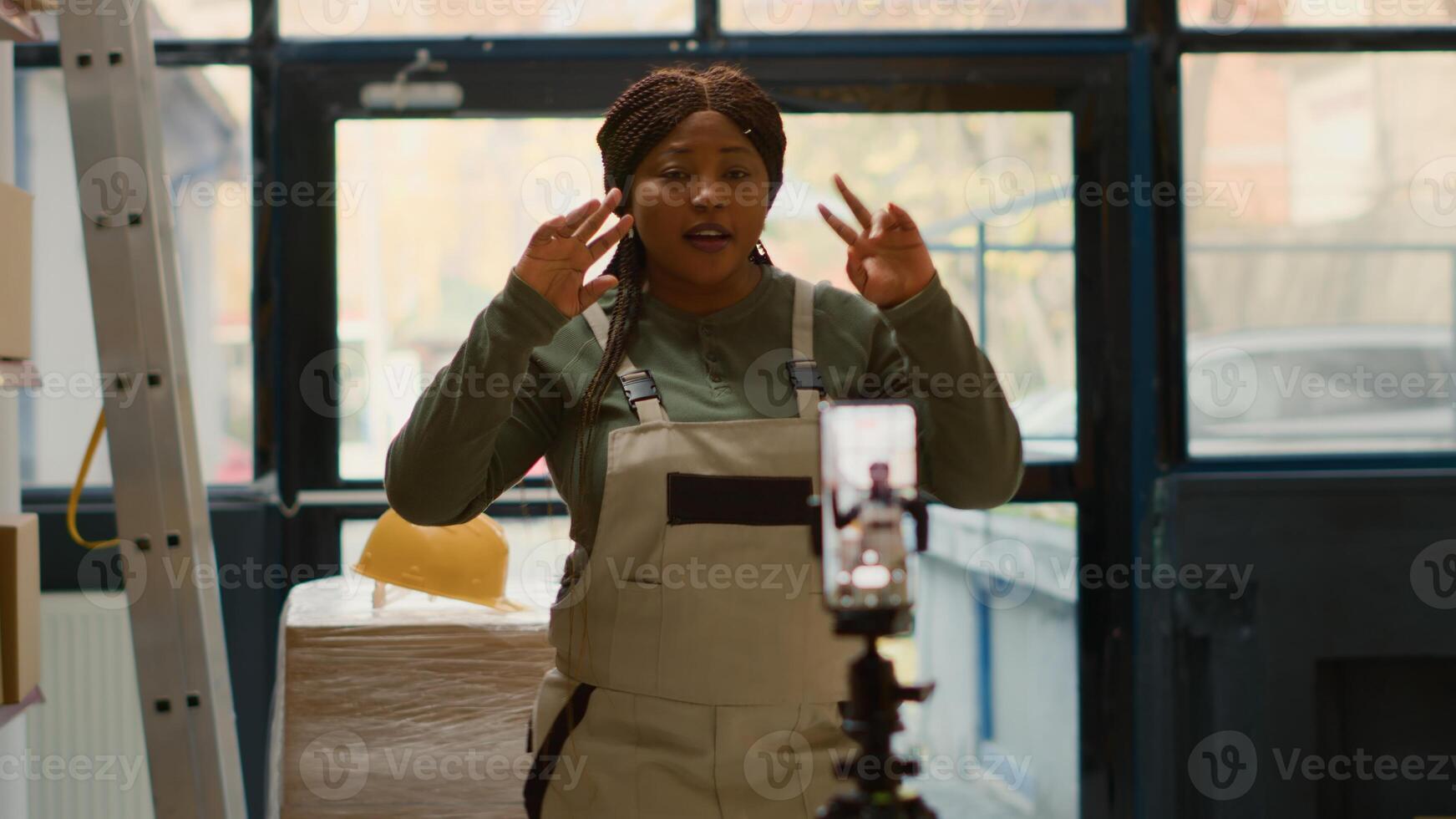 Warehouse employee using cellphone placed on tripod to make training video for interns. Worker filming herself in stockroom showing trainees how to store merchandise, dolly out shot photo