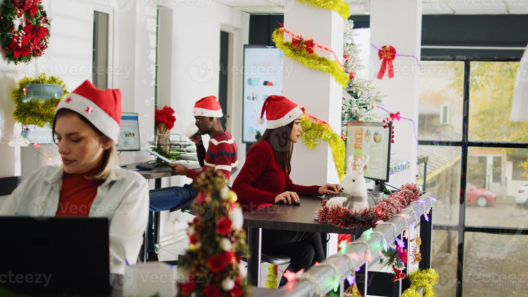 Hardworking multicultural employees working during Christmas season in festive decorated office. Diligent BIPOC coworkers inputing data on computers in diverse xmas ornate workplace photo
