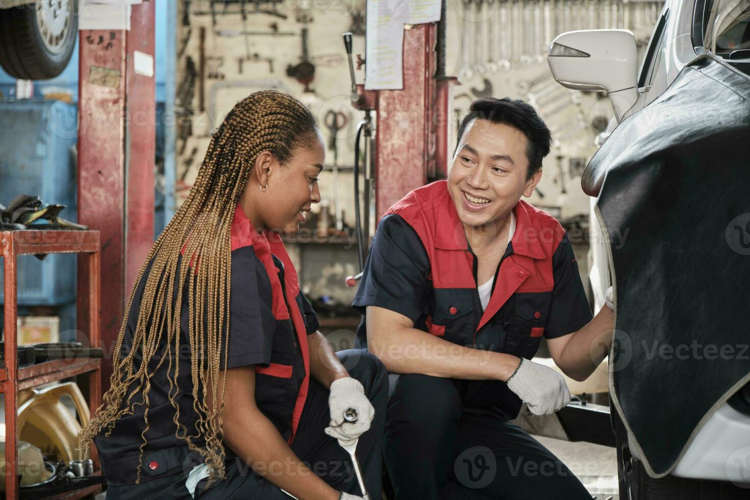 Professional male automotive supervisor trained Black female mechanic technician to screw car wheel nuts for repair at garage, vehicle maintenance service works industry occupation business jobs. photo