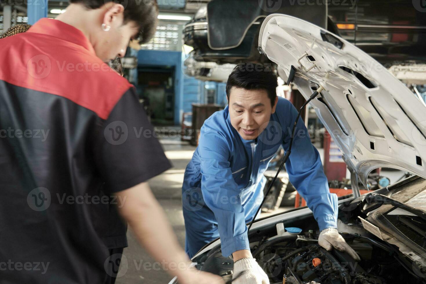 asiático masculino profesional automotor ingeniero supervisor describe coche motor mantenimiento y reparar trabajo con mecánico trabajador personal equipo en reparar Servicio cochera, especialista ocupaciones en auto industria. foto