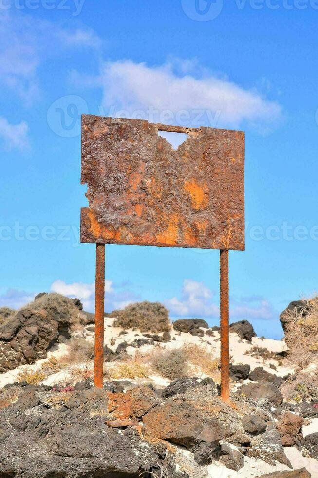 a rusty sign on the beach in the middle of the desert photo