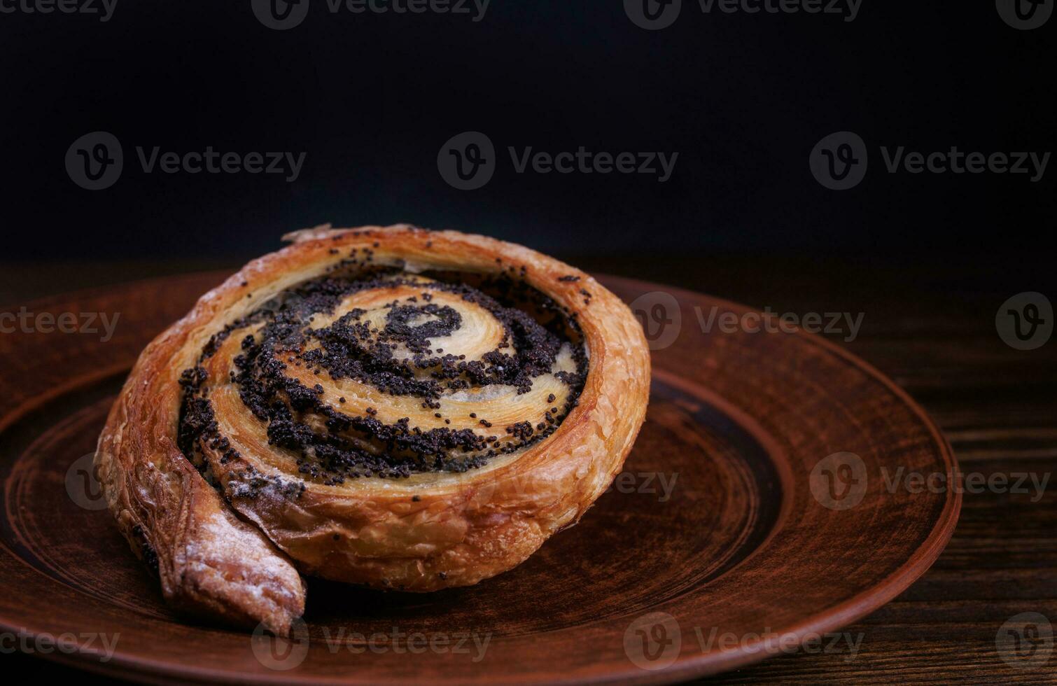 A delicious bun with poppy seeds lies on a clay plate. photo