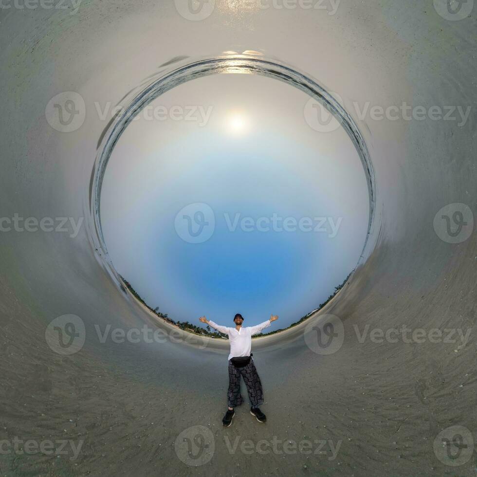 blue hole sphere little planet inside ocean seashore and sands withhappy man stands on coast in rays of evening tropical sun with transformation of spherical panorama 360 degrees. photo