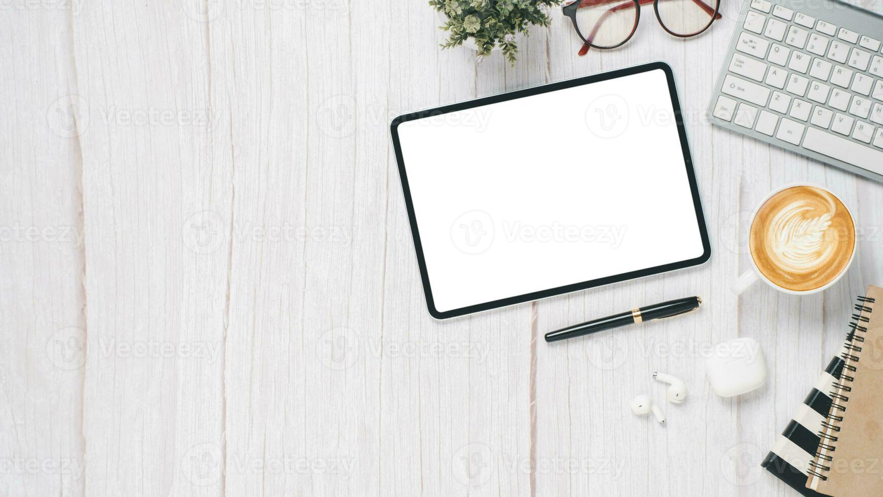 blanco de madera escritorio lugar de trabajo con blanco pantalla tableta, teclado, bolígrafo, lente, cuaderno y taza de café, parte superior ver plano laico con Copiar espacio. foto