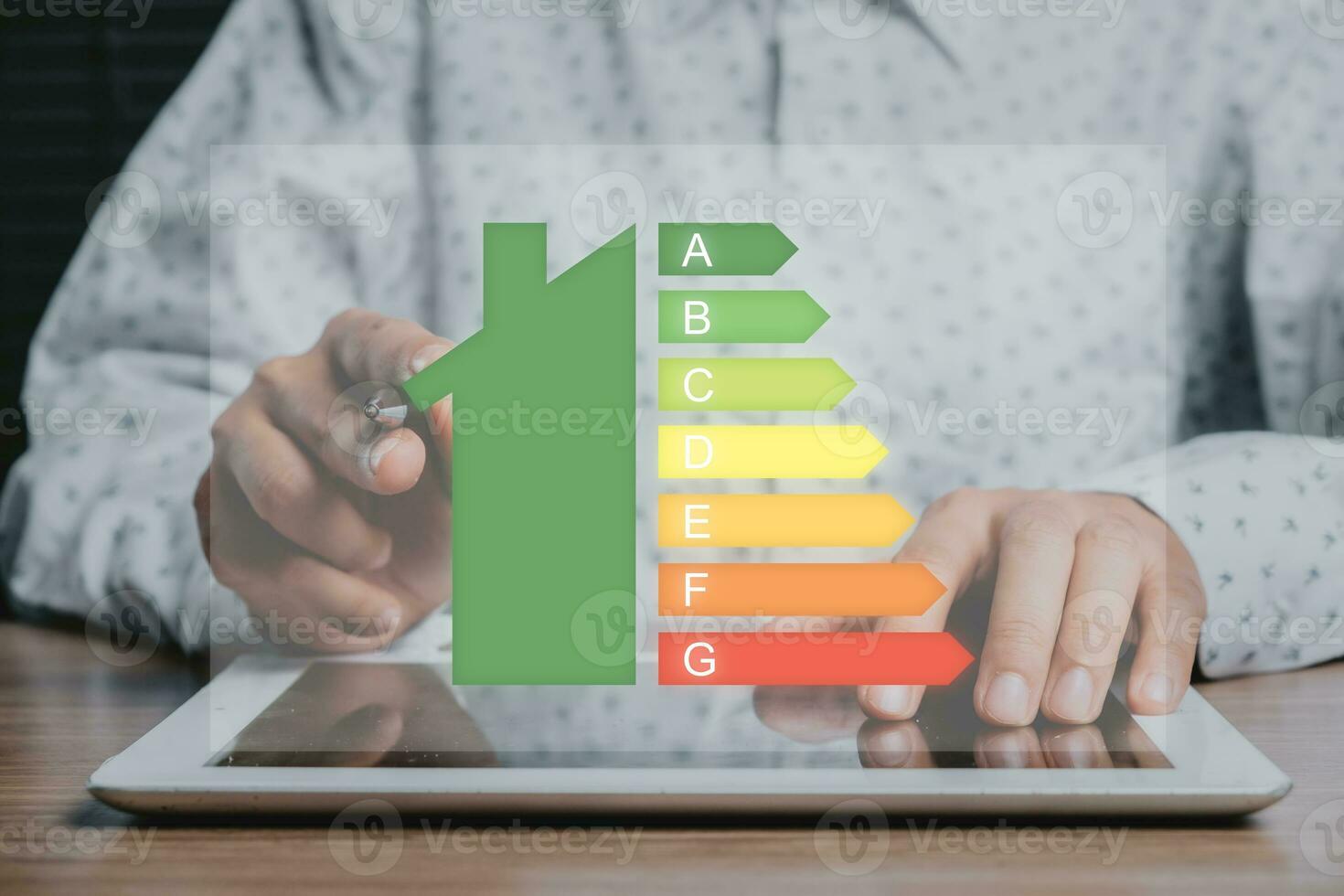 Person hand using digital tablet computer with house icon energy efficiency scale image on office desk, Concept of ecological and bio energetic house. Energy class. photo