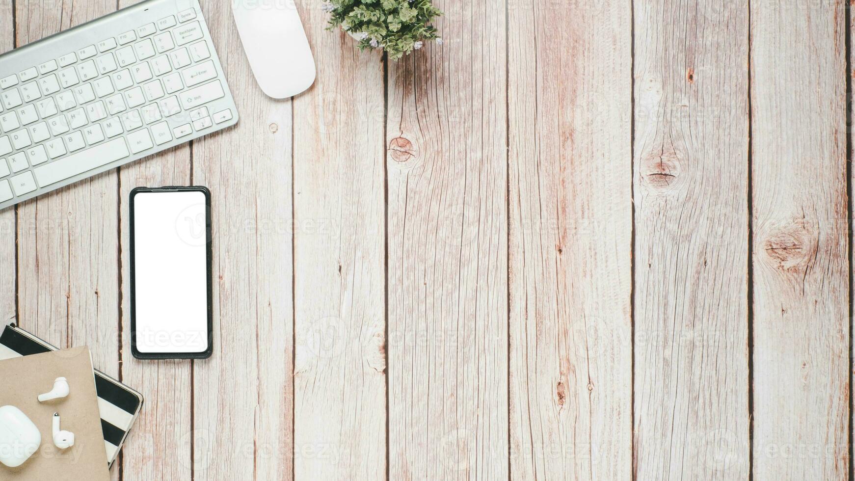 Wooden desk workplace with blank screen smartphone, keyboard, mouse, earphone and notebook, Top view flat lay with copy space. photo