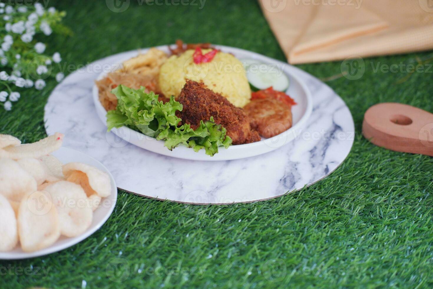 indonesian style yellow rice with minced chicken in white plate on green grass background photo