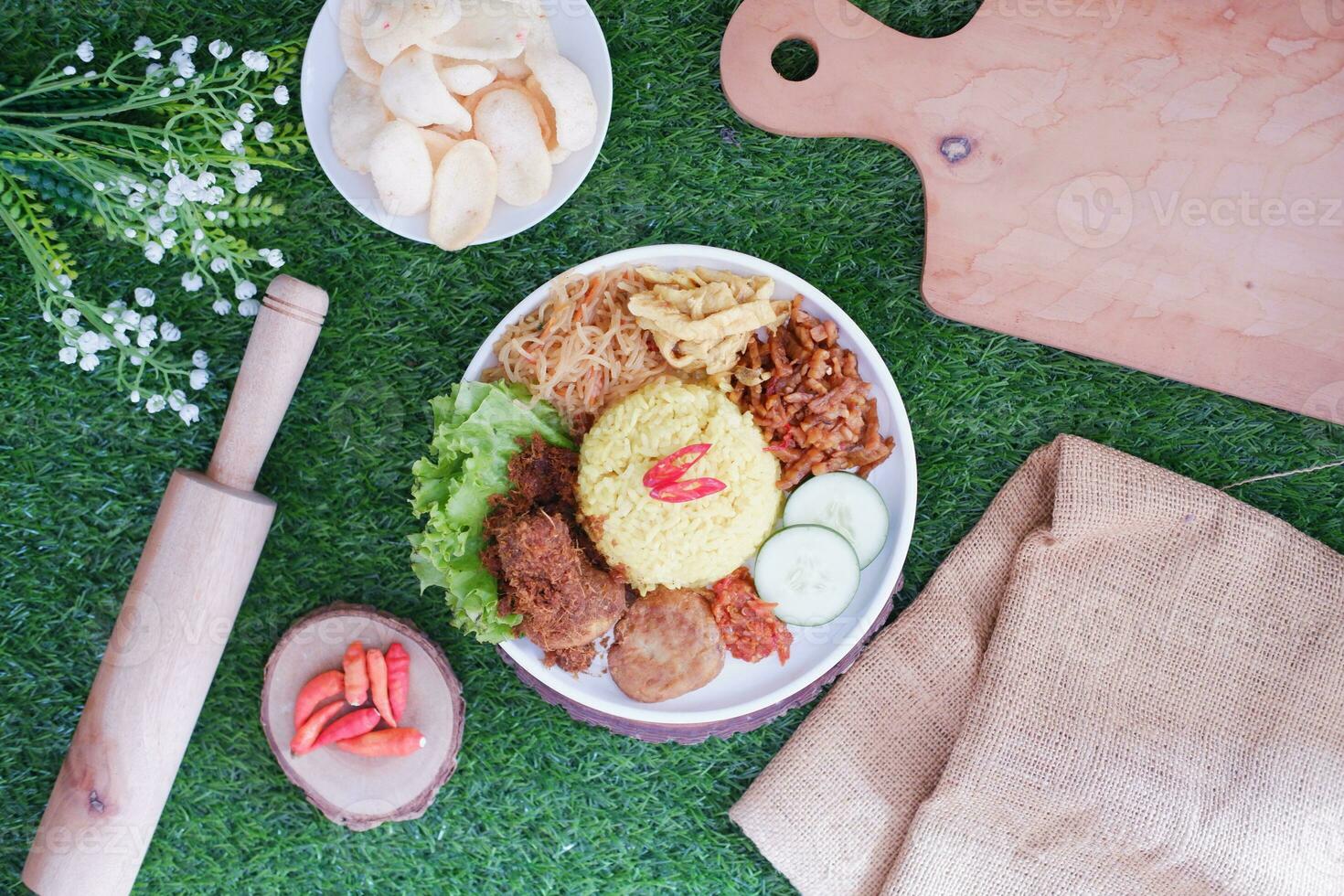 indonesian style yellow rice with minced chicken in white plate on green grass background photo