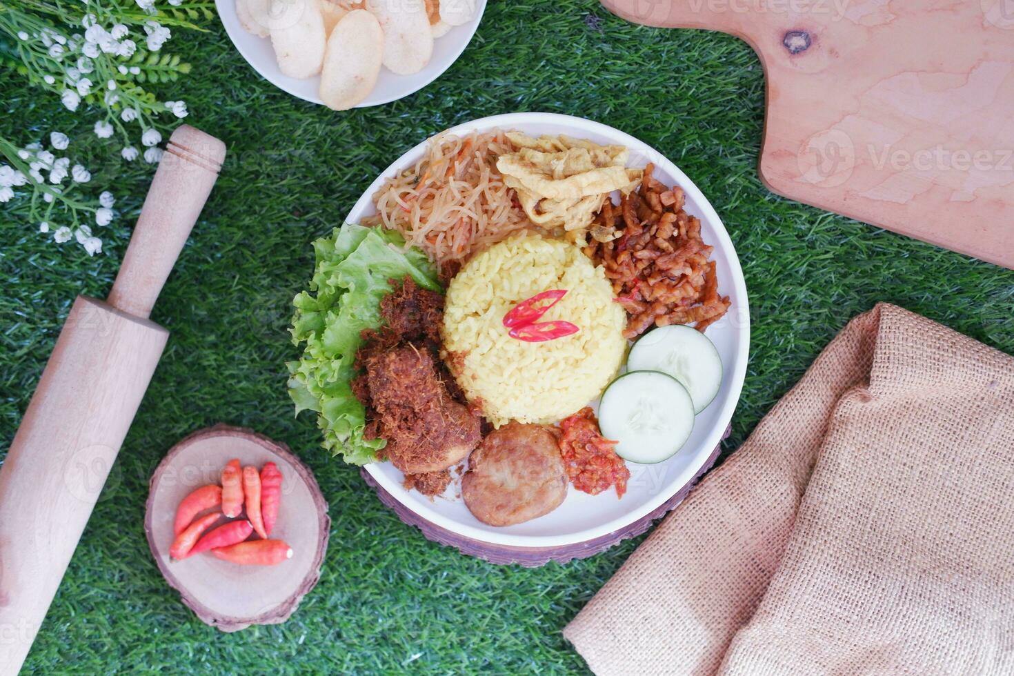 indonesian style yellow rice with minced chicken in white plate on green grass background photo