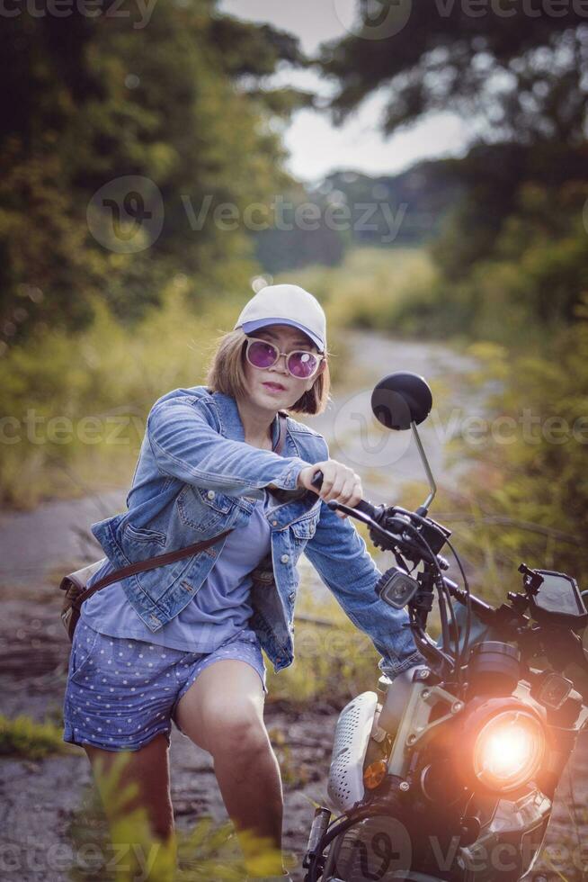 beautiful woman wearing blue jeans jacket sitting on enduro motorcycle against colorful natural  background photo
