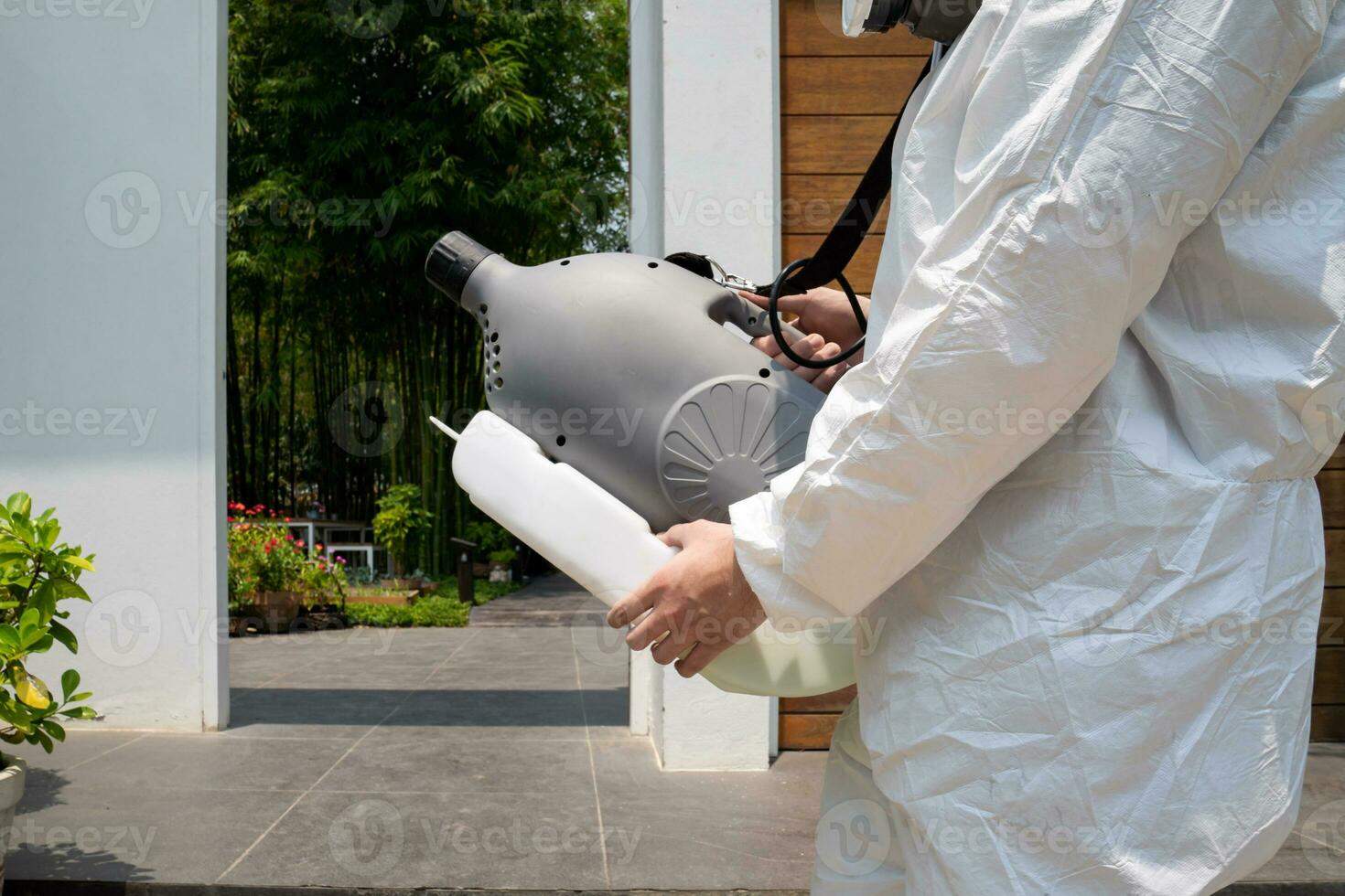 Professional technical man in prevention suit with his sterilizing machine and disinfecting water sprays in the outdoor field for purifying coronavirus COVID-19. photo
