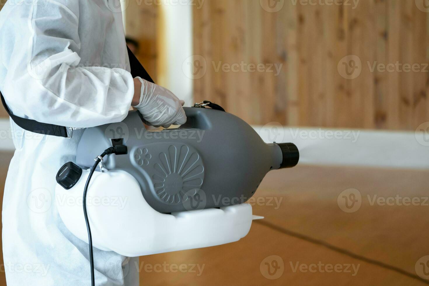 Professional technical man in prevention suit sprays sterilising solution by electrical spray machine on the wood floor and white background with studio light. photo