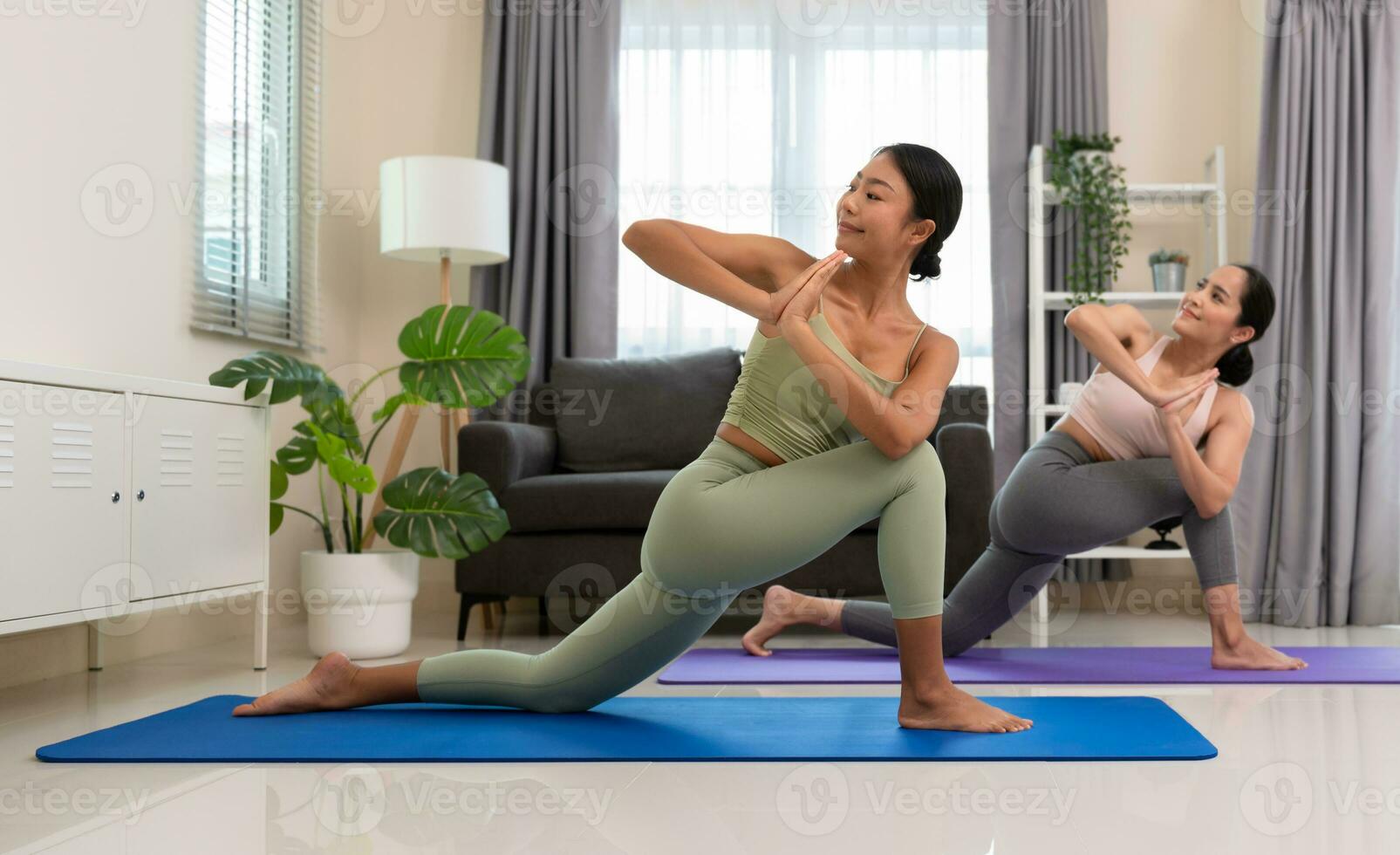 Two women doing yoga exercise at home, stretching in Parivrtta Anjaneyasana or Revolved Low Lunge Pose in  bedroom. Working out wearing sportive top and leggings. Relaxation and Healthcare concept. photo