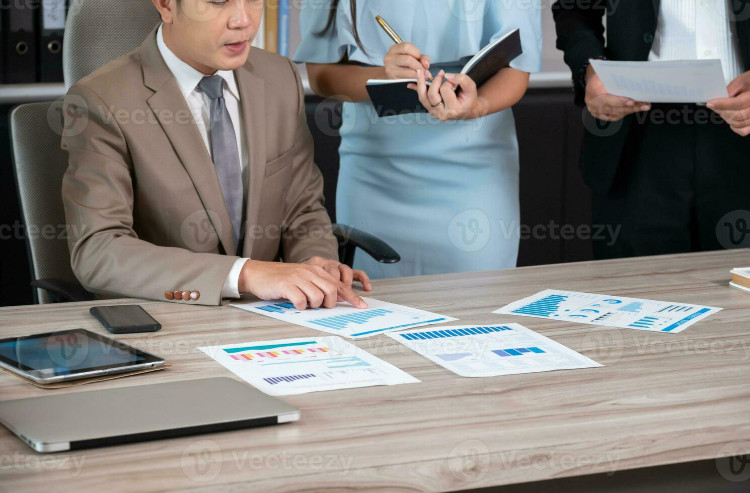 Businessman working on project startup presentation in team, comparing statistic data, studying values on graph diagrams while secretary making notes at office photo